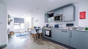 Cozinha moderna com armários cinza, micro-ondas e máquina de café. Há uma área de refeições com mesa e cadeiras.