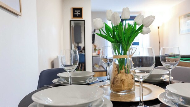 A dining table set with white plates, glasses, and a vase with white tulips. - Modern Liverpool Flat | Contractors & Work Trips % (Merseyside)