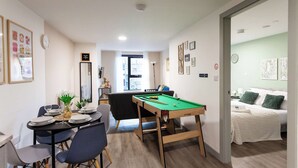 A compact living space with a dining area, a pool table, and a bedroom with a bed and green pillows. - Modern Liverpool Flat | Contractors & Work Trips % (Merseyside)