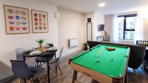 A pool table with a green felt surface, a clock on the wall, and framed pictures of cups on the wall. - Modern Liverpool Flat | Contractors & Work Trips % (Merseyside)