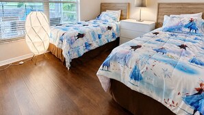 Ein Schlafzimmer mit zwei Betten, einem Nachttisch, einer Lampe und einem Fenster mit Jalousien.