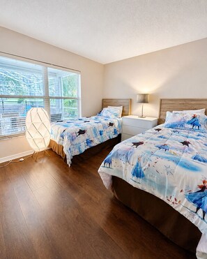A bedroom with two beds, a nightstand, a lamp, and a window with blinds. - Spacious 5-bedroom house with Private Pool (Haines City)