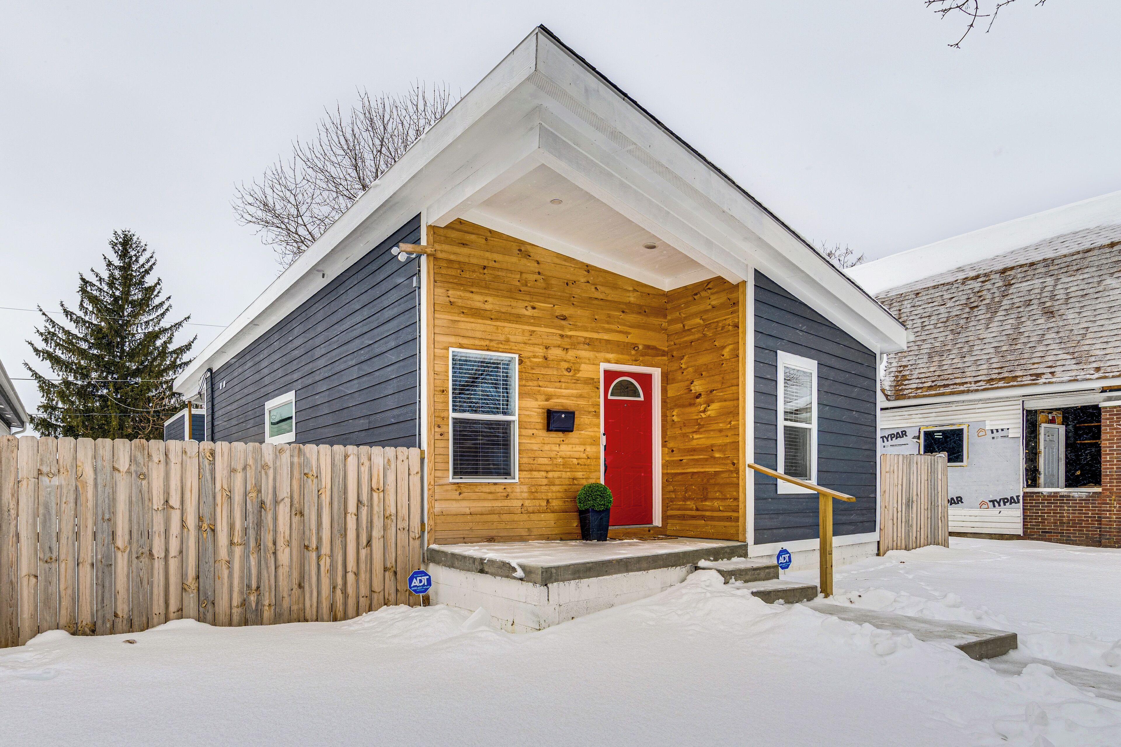 A small wooden house with a red door, a wooden fence, and a snow-covered ground.