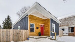 Una pequeña casa de madera con una puerta roja, una valla de madera y el suelo cubierto de nieve.