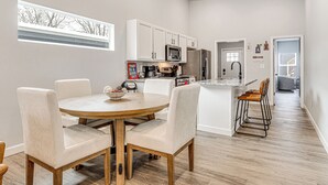 Una cocina moderna con armarios blancos, una isla central con taburetes y una mesa de comedor con sillas.