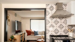 Eine moderne Küche mit einem Edelstahlherd, ein Essbereich mit einem Holztisch und ein Wohnzimmer mit einer Couch und einem Fernseher.
