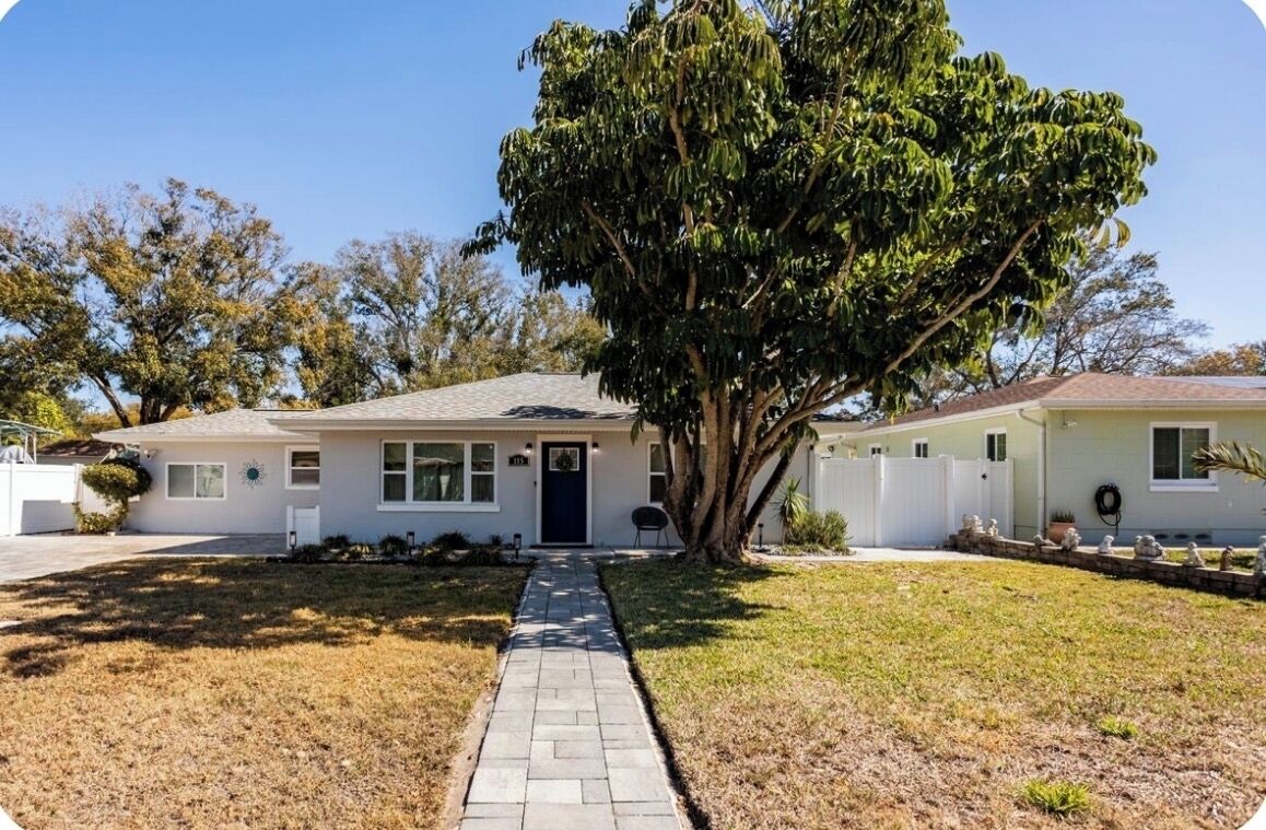 A single-story house with a front yard, a pathway leading to the front door, and a large tree in front.
