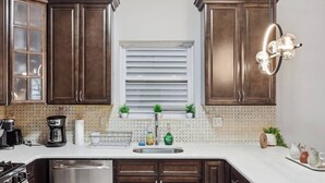 Una cocina con armarios de madera oscura, una encimera blanca, un lavamanos de acero inoxidable, una cafetera y un escurreplatos.