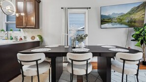 Un comedor con una mesa de madera oscura, sillas blancas y un ventanal con persianas.