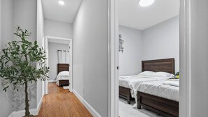 Un pasillo que conduce a un dormitorio con piso de madera, paredes blancas y una planta en maceta.