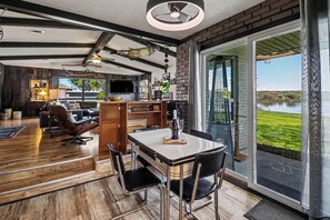 A spacious living area with a dining table, chairs, and a view of a lake through large glass doors.