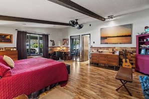 A bedroom with a bed, a desk, a guitar, and a view of the outdoors.