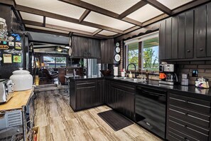 A modern kitchen with dark cabinetry, stainless steel appliances, and a large window.