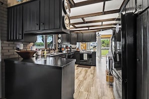 A kitchen with dark cabinetry, a central island, and a large refrigerator. - Portage Lake Family Getaway - 200ft Frontage! (Onekama)