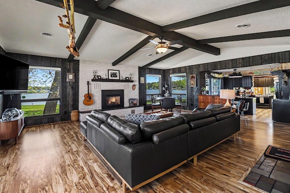 A spacious living room with a large black leather sofa, a fireplace, and a view of the outdoors.