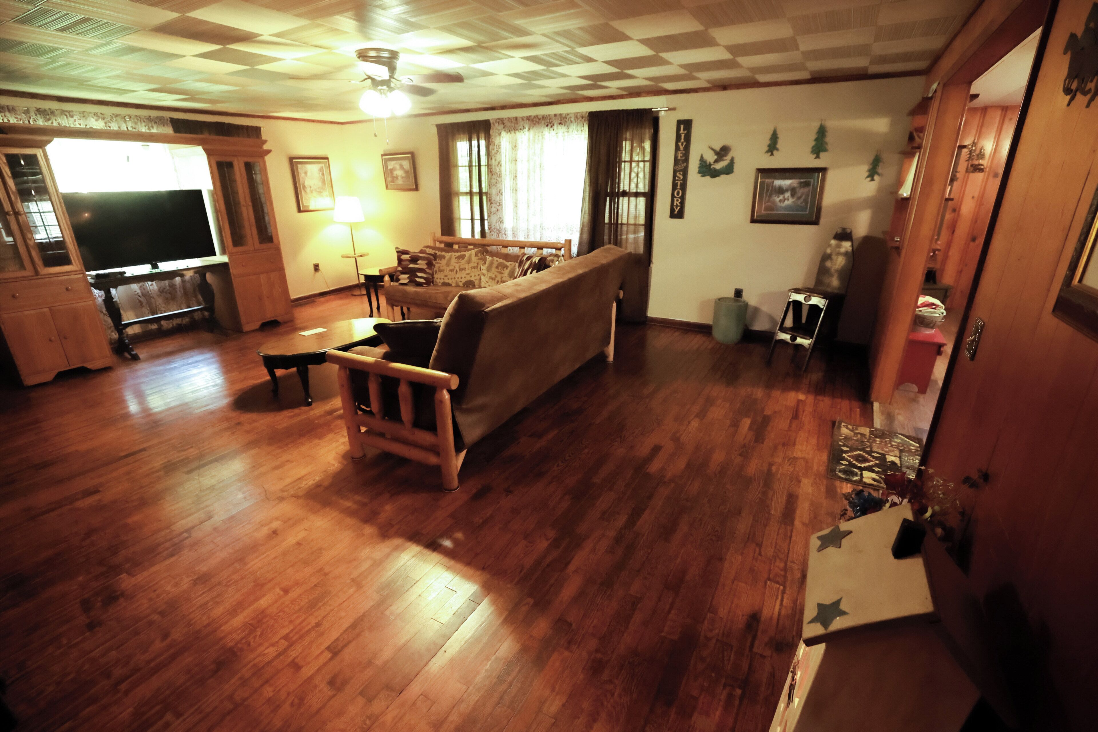 A living room with a wooden floor, a sofa, a television, and a ceiling fan.