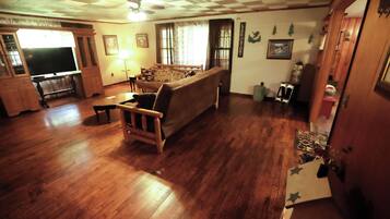 A living room with a wooden floor, a sofa, a television, and a ceiling fan.