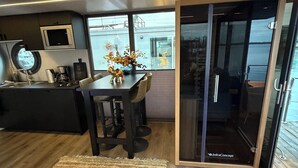 A modern kitchen with a microwave, coffee maker, and a dining area with a table and chairs. - Exclusive Houseboat 12 x 5 m with sauna and hot tub (Maasbommel)