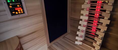 A room with a wooden panel wall, a control panel with green and red lights, and a wooden staircase with red lights.
