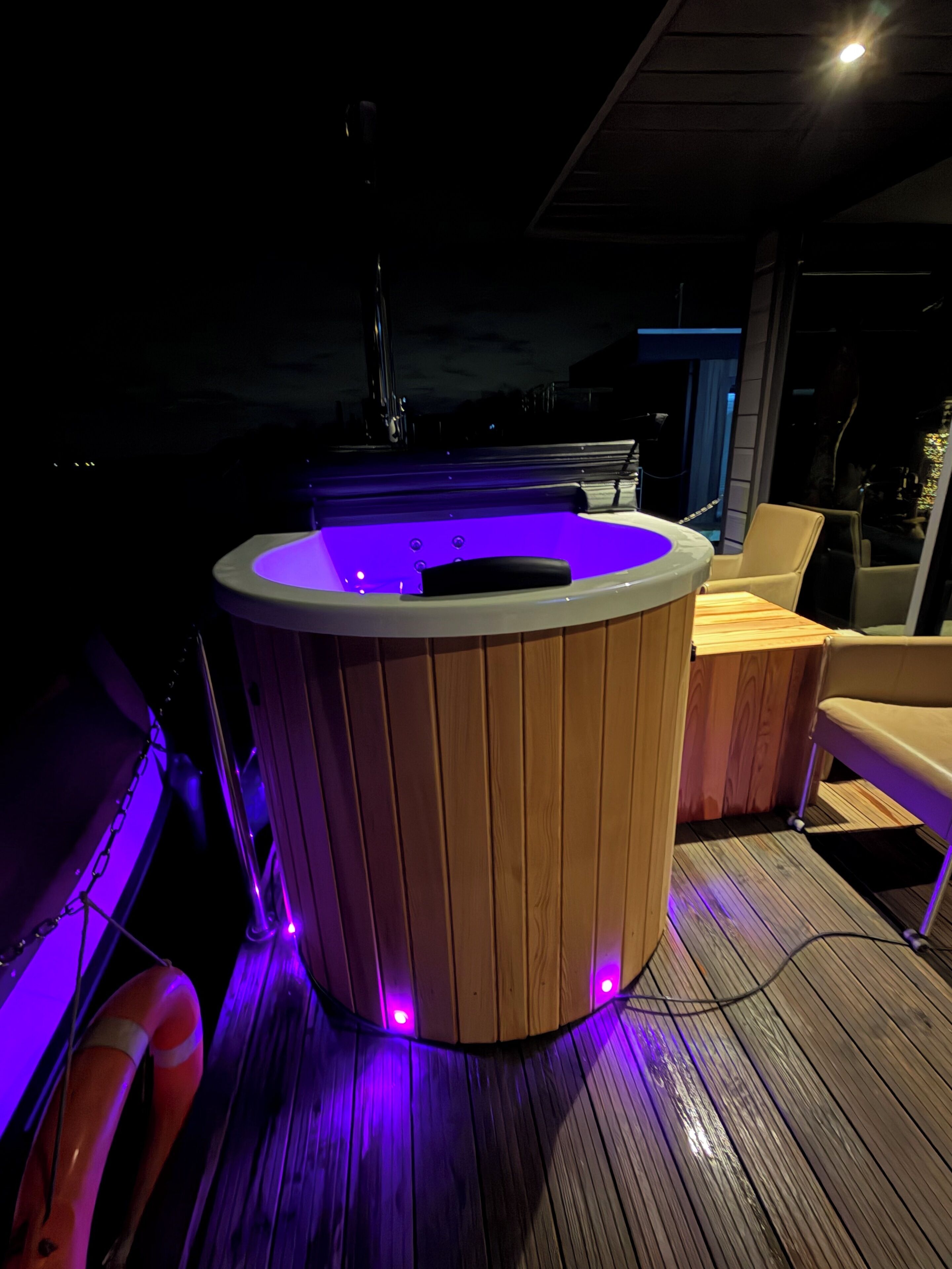 Ein Whirlpool mit Holzverkleidung und violetter Beleuchtung auf einer Holzterrasse.