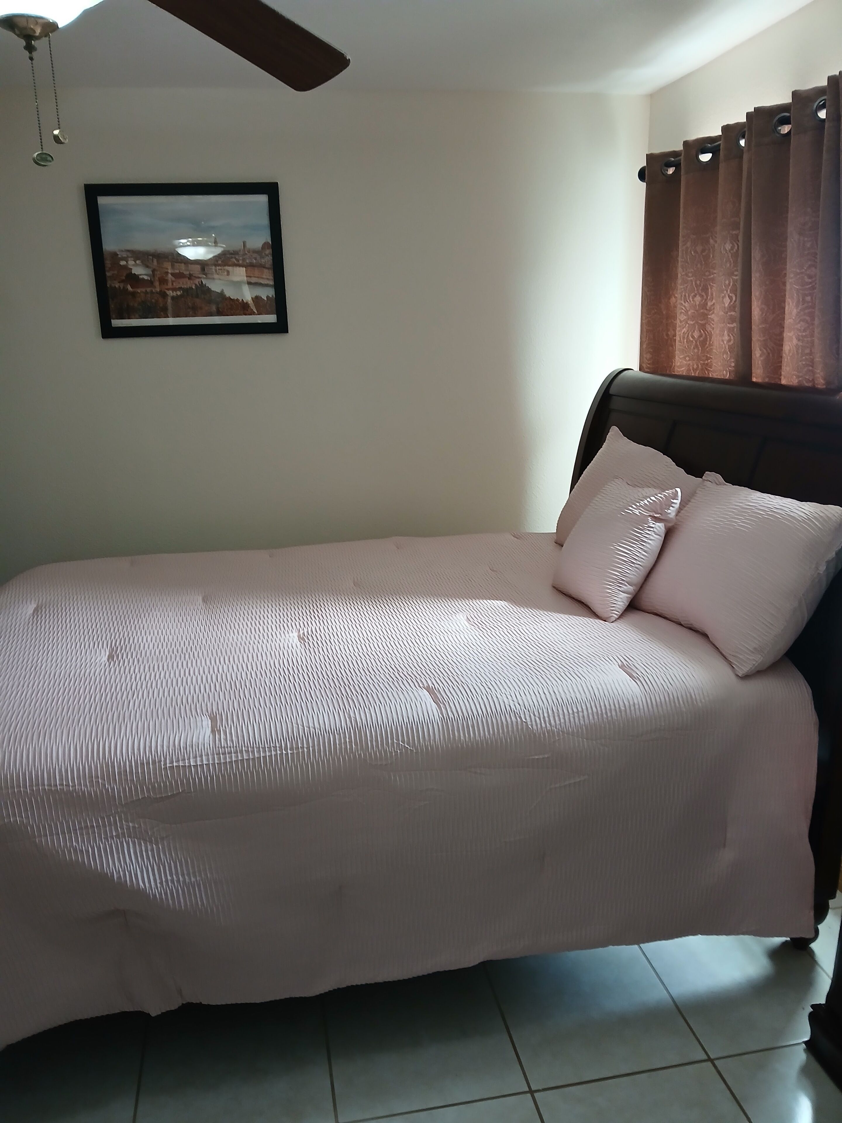 A bedroom with a bed, a ceiling fan, a framed picture on the wall, and curtains.