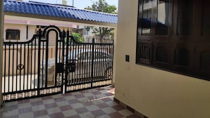 A gated entrance with a checkered floor, a balcony with a blue roof, and a building with a dark wooden door.