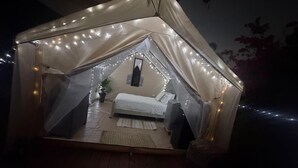 Alojamiento en tienda de campaña con cama, una mesita y luces colgantes.