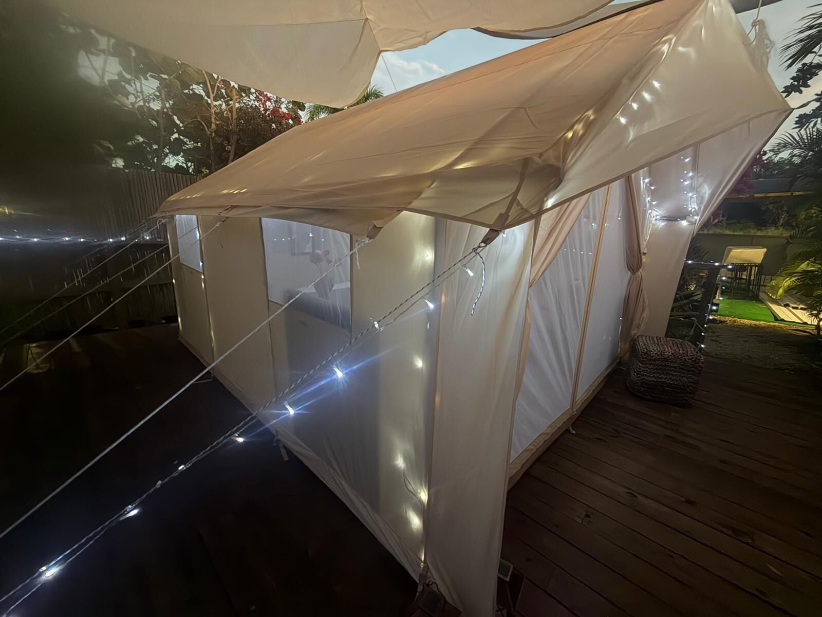 Una estructura tipo tienda con luces colgantes, una terraza de madera y vistas a un jardín.