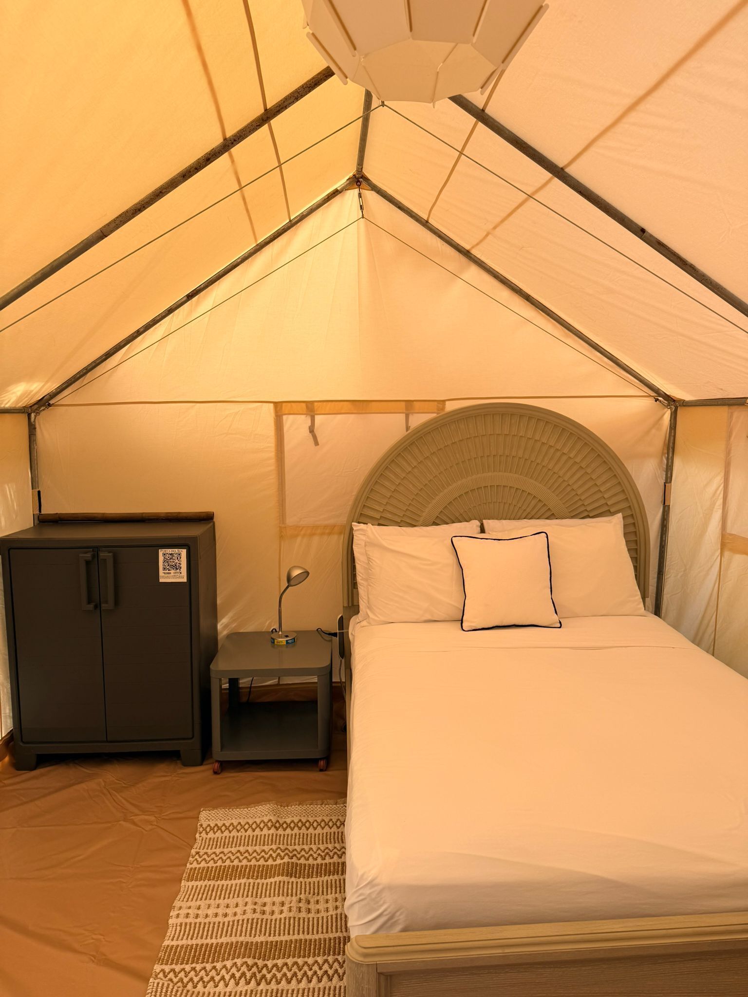 Een tentkamer met een bed, een kledingkast en een kleine tafel met een lamp.