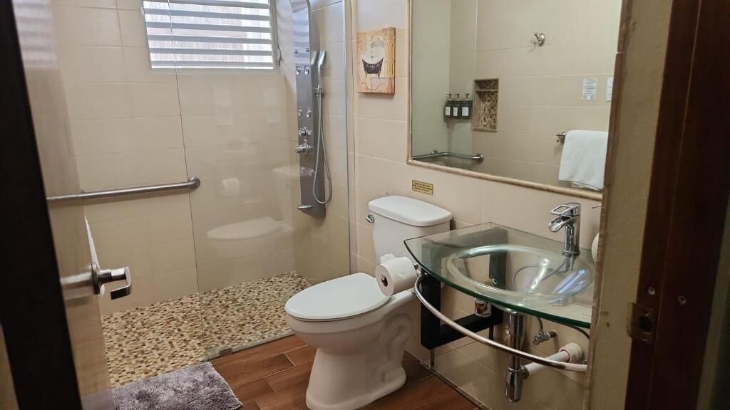 Un baño con un lavabo de vidrio, inodoro y ducha.