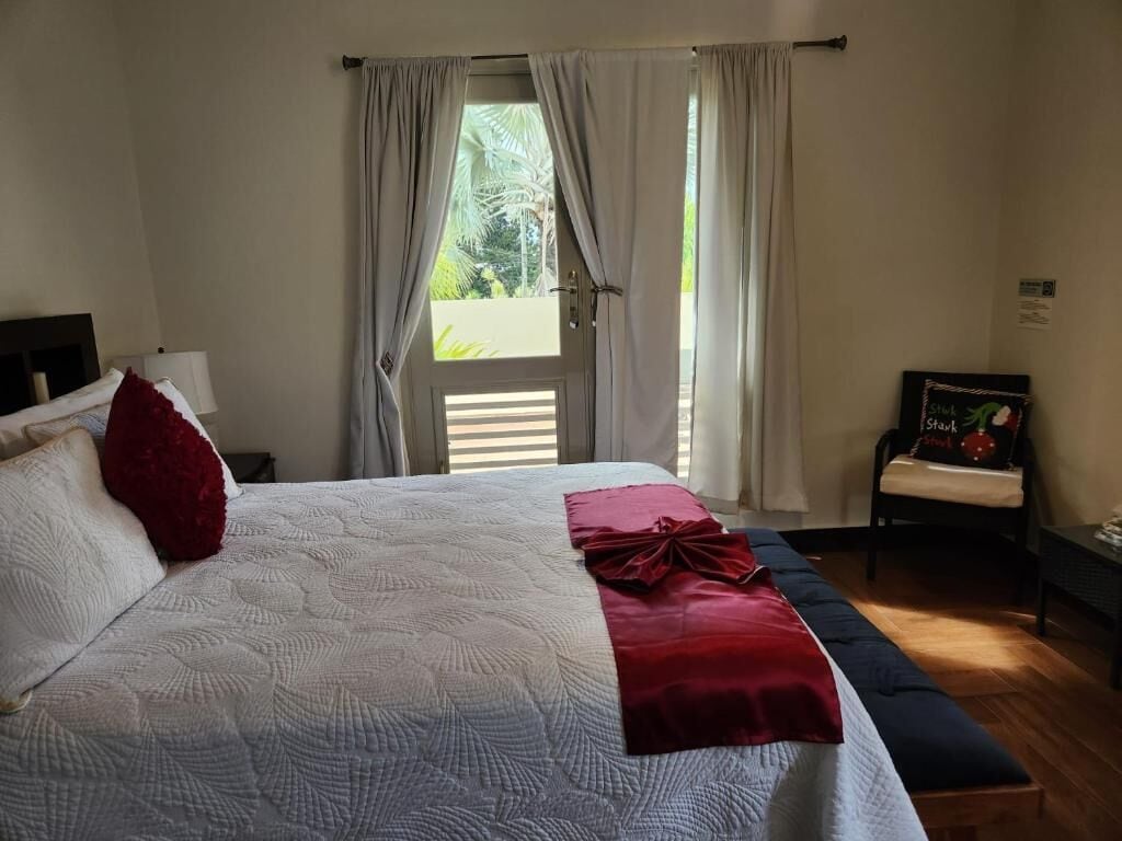A hotel room with a bed, a bench, a chair, and a window with curtains.