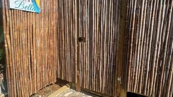 Una cerca de bambú con un letrero de bienvenida y un sendero de piedra que conduce a un edificio.