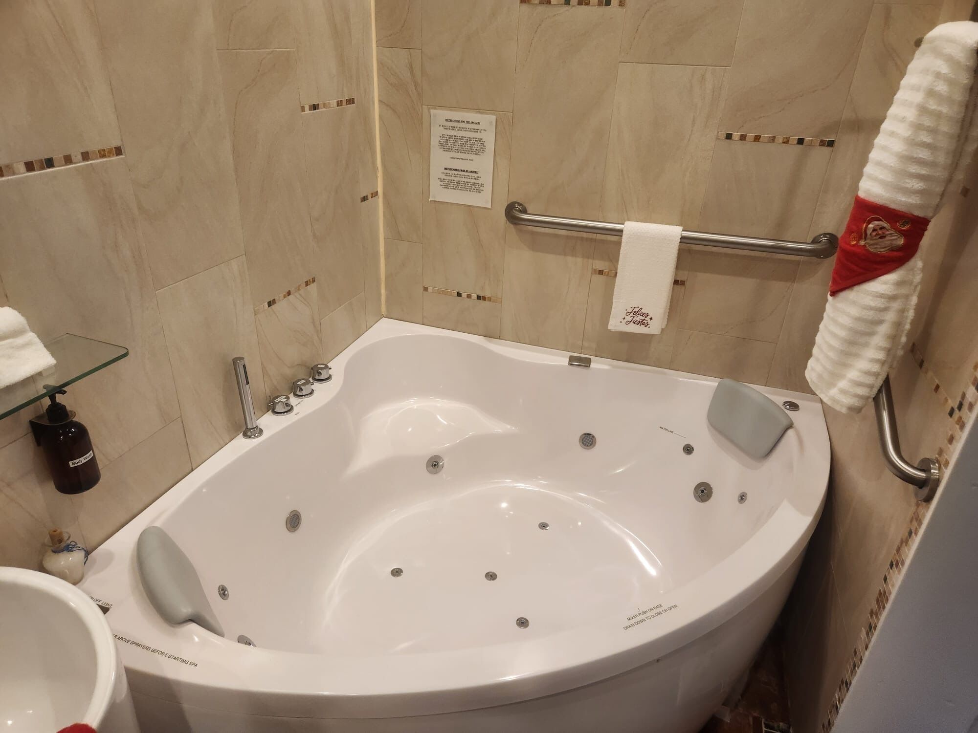 Une salle de bain avec une grande baignoire, une étagère en verre, un flacon de gel douche et un porte-serviettes avec une serviette rouge.