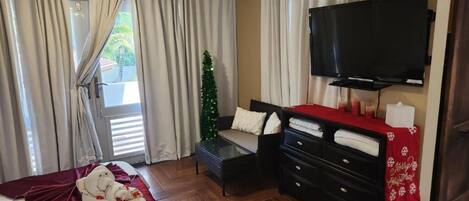 Una camera d'albergo con un letto, una TV, una scrivania, una sedia, un comò e un albero di Natale.