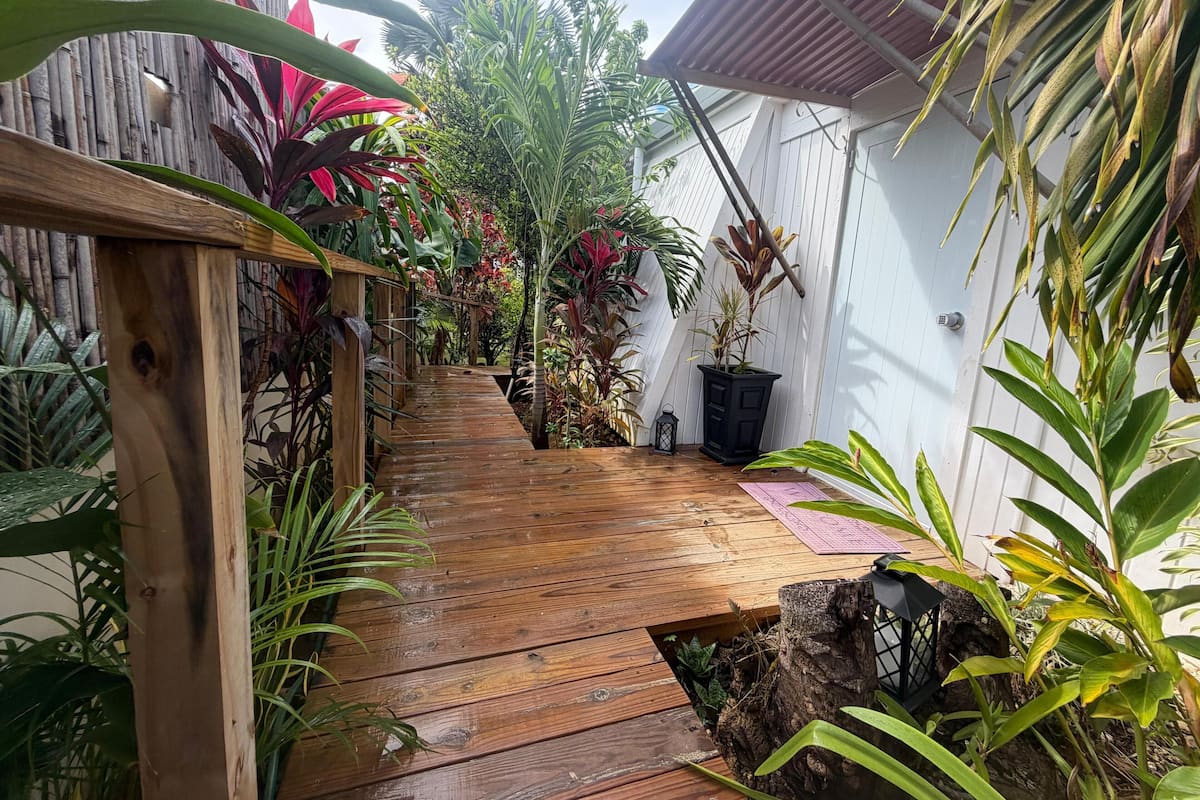 A wooden pathway leading through a lush garden area with various plants and a small black lantern.