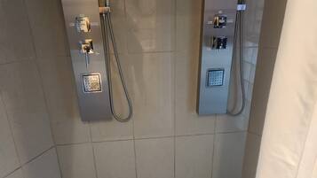 En duschhörna med kaklade väggar och golv, där golvet har ett geometriskt mönster och det finns kontrollpaneler för vattentemperatur och vattenflöde.