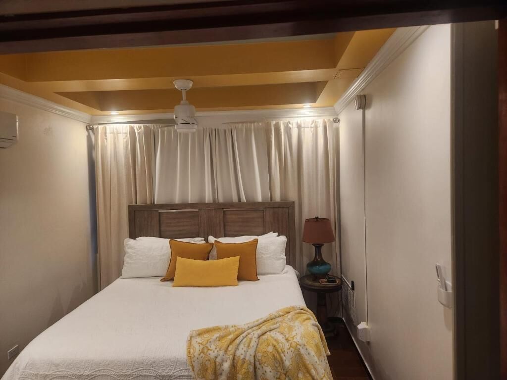 Una habitación de hotel con cama, cortinas, lámpara y ventilador de techo.
