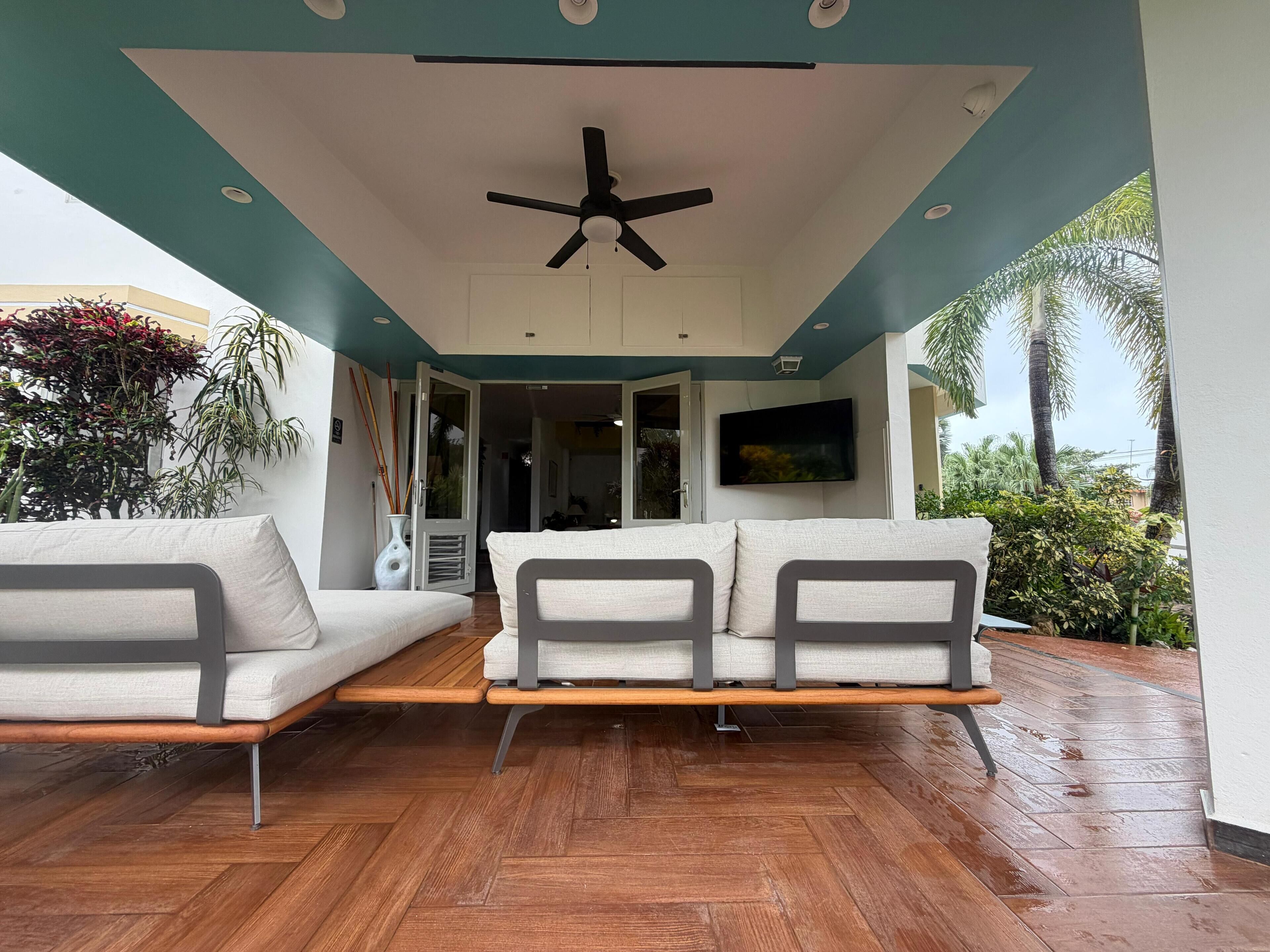 Un espacio exterior moderno con zona de estar, ventilador de techo, suelo de madera y vistas al exterior.