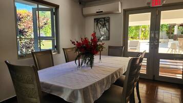 Un comedor con una mesa lista para cuatro personas, un jarrón de flores rojas y vistas al exterior a través de un ventanal.