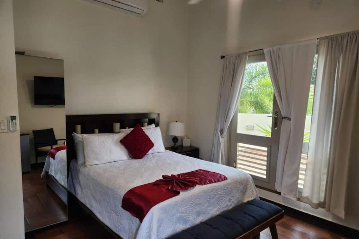 A hotel room with a bed, bedside tables, a TV, and a window with curtains.