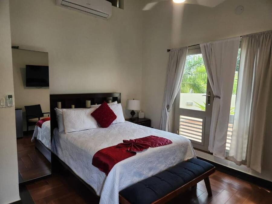 A hotel room with a bed, bedside tables, a TV, and a window with curtains.
