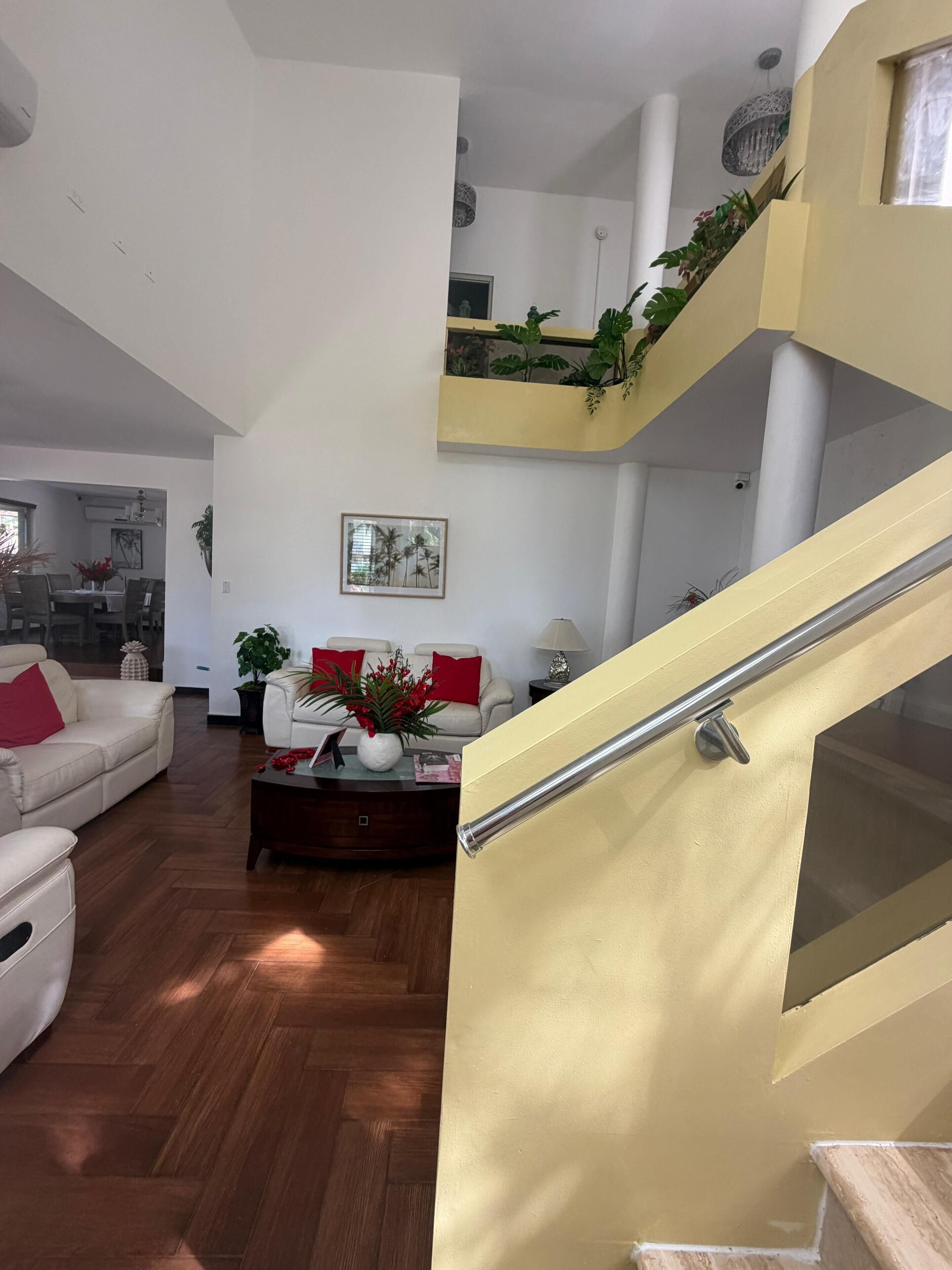 Un amplio salón con techo alto, una escalera con barandilla de cristal y vista al comedor.