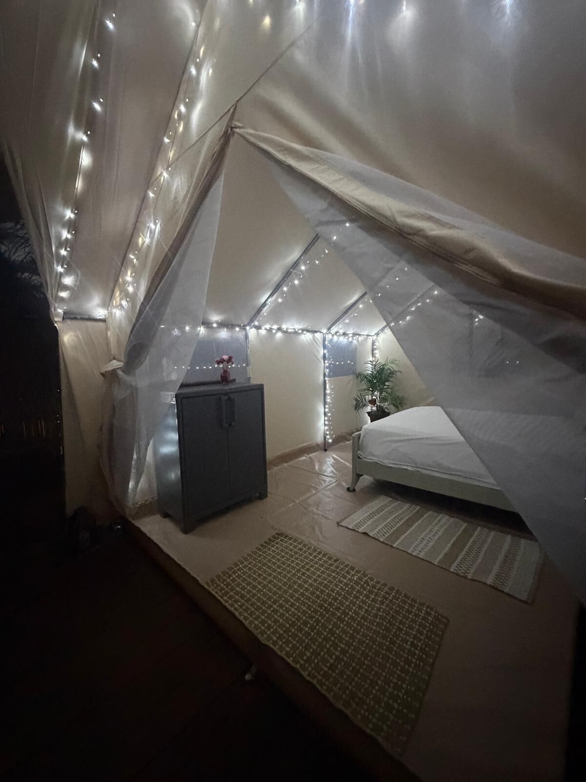 Una carpa con una cama, un mueble pequeño y luces de cuerda.