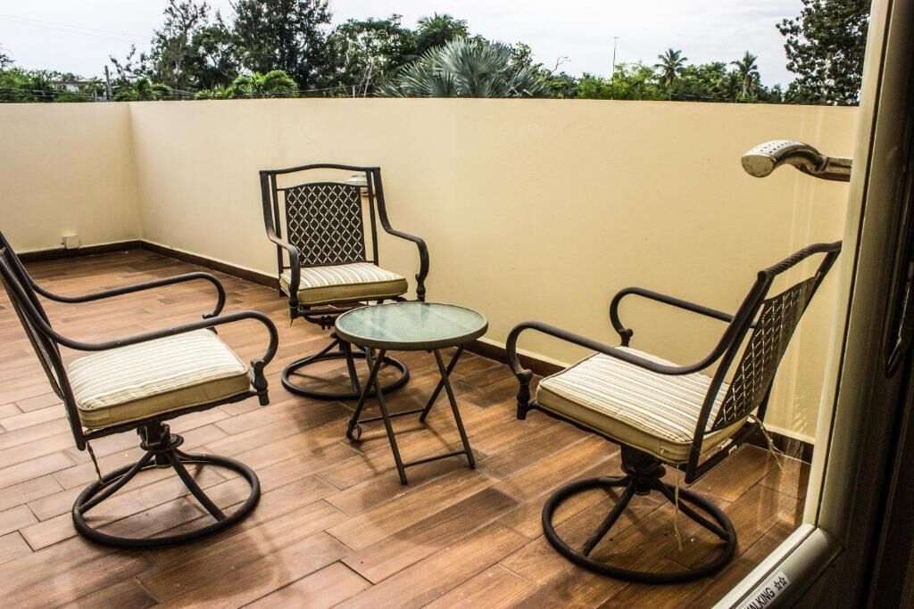 A balcony with two chairs and a small table, wooden flooring, and a view of trees and buildings in the background.