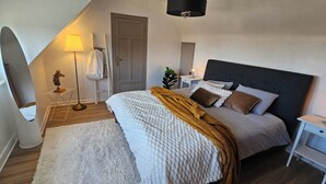 Een slaapkamer met een bed, nachtkastjes, een lamp, een radiator, een deur en een raam.