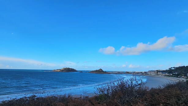 Een kustlandschap met een strand, helderblauwe lucht en verafgelegen rotsformaties.