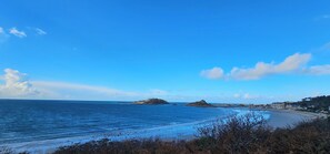 Eine Küstenlandschaft mit Strand, blauem Himmel und fernen Felsen.