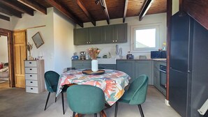 Een kleine keuken met een eettafel, stoelen, kastjes en een koelkast.
