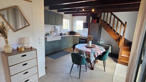 Een keuken met blauwgroene kastjes, een eettafel met stoelen, een vaas met bloemen en een trap.