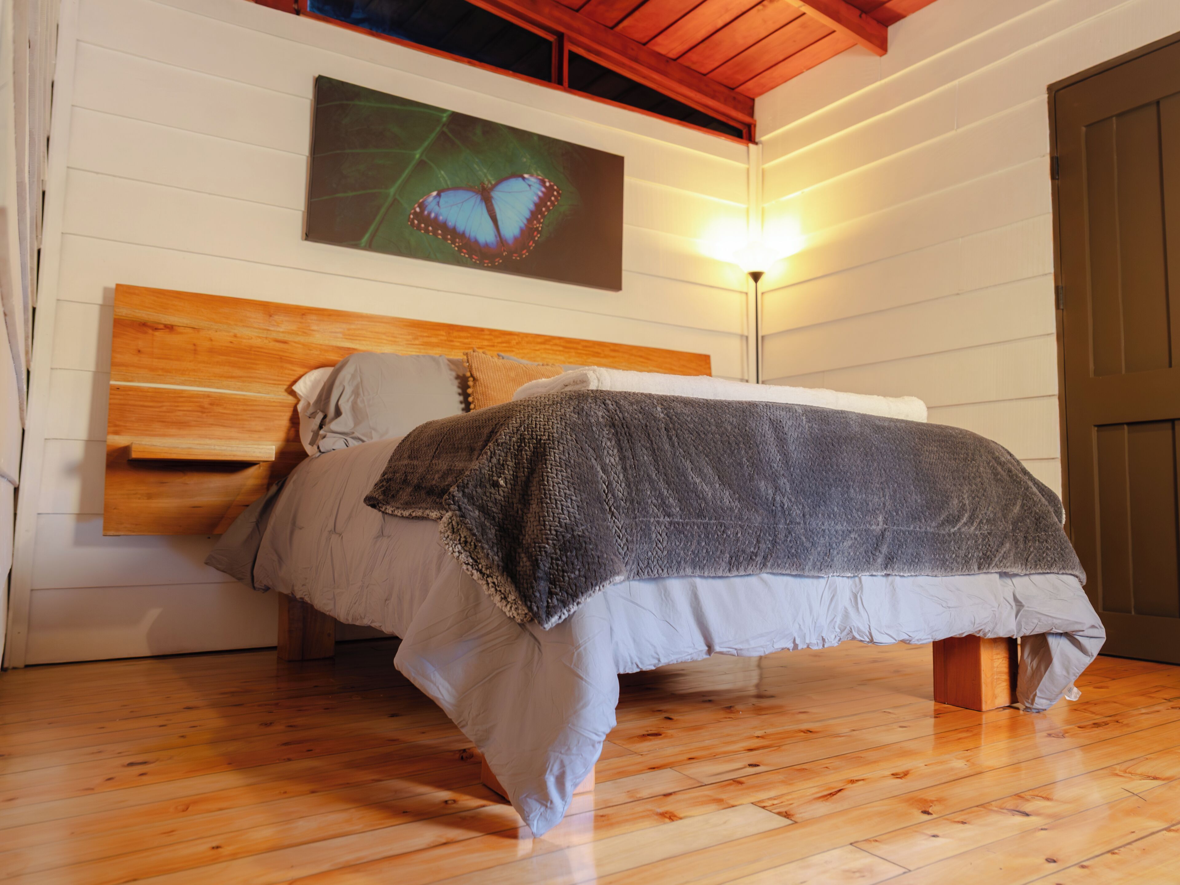A bed with a wooden headboard, a gray blanket, and a wall-mounted picture of a butterfly.